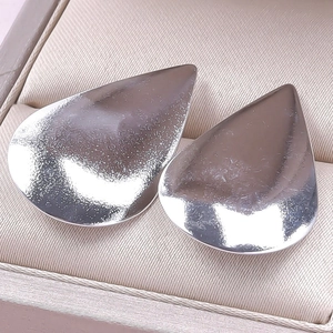 Macro view of polished silver teardrop earrings resting in a soft beige jewelry box