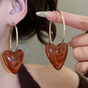 Close-up of golden hoop earrings featuring amber resin heart charms worn by a model