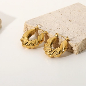 Detailed close-up of gold-plated stainless steel twisted hoop earrings on raw stone