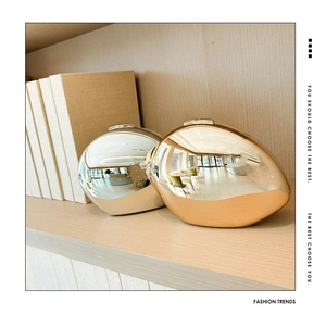 Glossy gold and silver oval metal clutch bags on a wooden shelf with fashion books