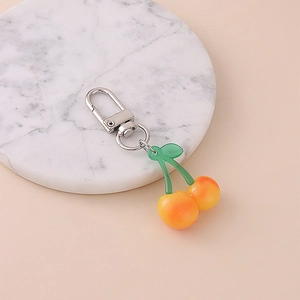 Cute orange gradient cherry keychain with green leaves on white marble surface