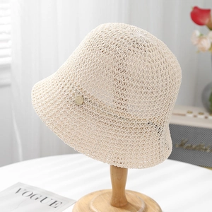 Close-up of cream knit bucket hat with hollow crochet design and round metal logo