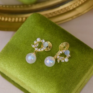 Detailed shot of golden cat eye earrings with pearls and zircon on green velvet