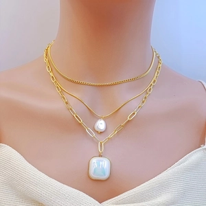 Close-up of layered gold snake chain necklace with pearl and square opal heart pendants