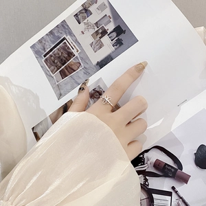 Close-up of adjustable silver hollow flower ring worn on index finger with fashion magazine