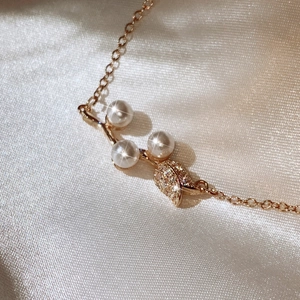 Close-up of pearl necklace with rhinestone-studded leaf pendant on gold chain