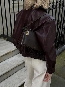 Close-up of deep brown leather shoulder bag with metal buckle on a fashion model