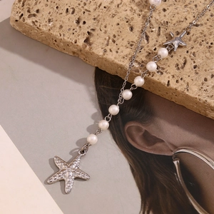 Detailed shot of silver starfish necklace with white pearls on a textured rock surface