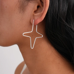 Close-up of minimalist silver star-shaped hoop earrings worn by a model on white background