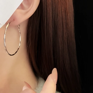 Close-up of minimalist silver hoop earring worn by a model showcasing polished metal texture