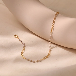 Detail of gold beaded bracelet featuring rectangular links and lobster clasp on beige fabric