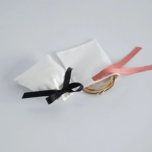 Detail of small white velvet jewelry pouches with black and coral pink ribbons and gold bracelet