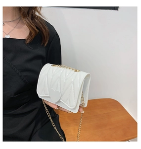 Detail of white quilted heart crossbody bag with gold chain strap held by a model