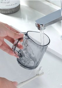 Gray translucent bathroom cup with ergonomic handle and toothbrush under running water