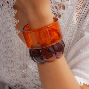 Detailed macro view of marbled orange and dark amber resin bangles against a white lace top.