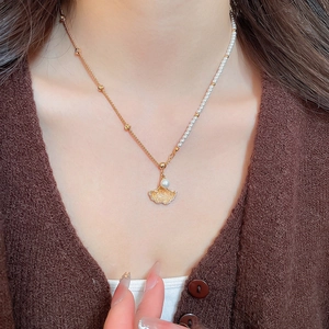 Detailed close-up of a gold maple leaf necklace with pearls on an asymmetrical chain