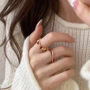 Detail of vintage gold twisted rings with red enamel hearts on hand with white sweater