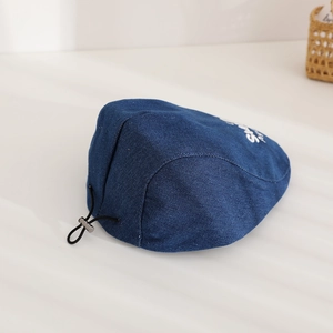 Detail of blue denim beret showing embroidery and adjustable metal buckle on back