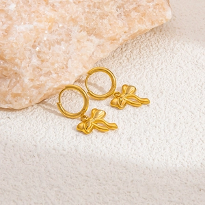 Detailed shot of gold-plated butterfly bow charms on hoop earrings against a stone background