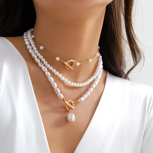 Detailed layered necklace featuring Baroque pearls and gold T-bar toggle chains on model