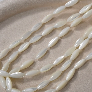 Natural white oval shell beads for DIY jewelry making displayed on a beige fabric base