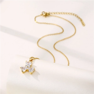 Collana a quadrifoglio dorata con zirconi cubici a cuore su sfondo bianco testurizzato