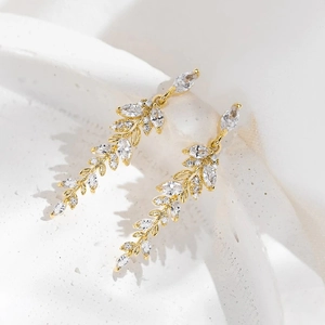 Detailed view of gold leaf drop earrings with marquise-cut zircons on a white stone base