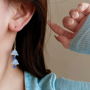 Close-up of blue lily-of-the-valley tassel earrings with gold hooks worn by a model