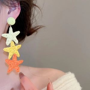 Detail of colorful raffia woven star tassel earrings shown on model for resort style