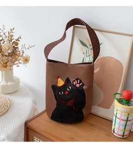 Detailed close-up of brown canvas bucket bag with lucky cat embroidery on a wooden table
