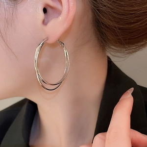 Gros plan de boucles d'oreilles doubles anneaux argentés portées par un mannequin chic