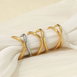 Minimalist stainless steel criss-cross rings in gold and silver on soft white fabric