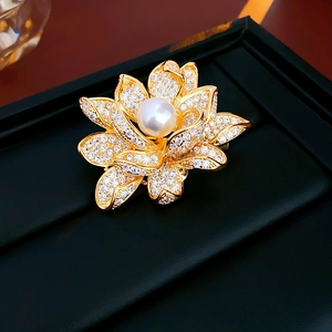 Macro shot of gold-plated lotus brooch with white zircons and center pearl on black leather