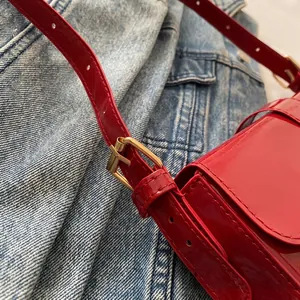 Detail of red patent leather shoulder strap with adjustable golden metal buckle and holes