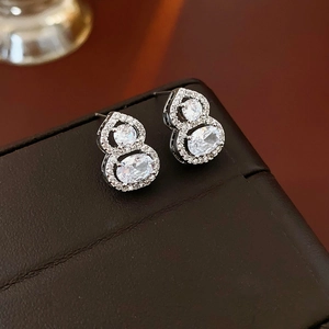 Macro shot of silver gourd-shaped earrings with sparkling cubic zirconia on leather case