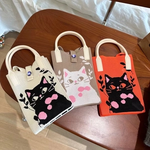 Trois mini sacs en tricot avec motifs de chat posés sur une chaise en bois naturel