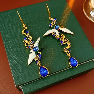 Detail of vintage gold earrings with white crane motif and blue teardrop gemstones