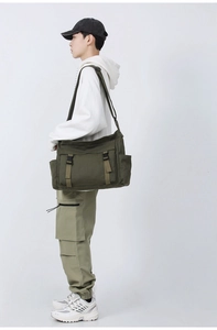 Vue latérale du sac messager en toile vert armée porté montrant la capacité et la sangle