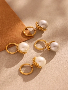 Detailed top view of 18k gold plated pearl earrings in white and grey on textured surface