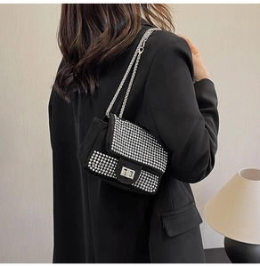 Close-up of black rhinestone shoulder bag with silver chain strap worn by a model