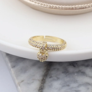 Macro detail of a golden heart charm ring with pave-set zircons on marble surface
