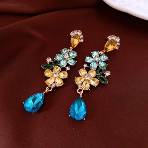 Close-up of golden floral earrings with blue crystals and vintage teardrop pendants