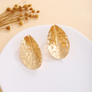Detail of gold hammered metal leaf earrings on a white plate with floral accents