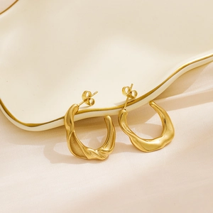 Detailed view of gold plated twisted C-shape hoop earrings on a ceramic dish