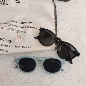 Kids round silicone sunglasses in black and mint green on a pebble texture backdrop