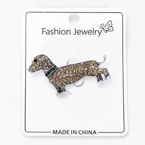 Detailed view of silver dachshund dog brooch with yellow and green crystals on card