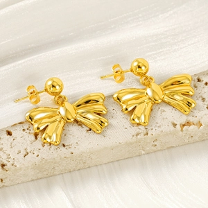 Elegant gold bow earrings with polished finish on cream travertine and silk background