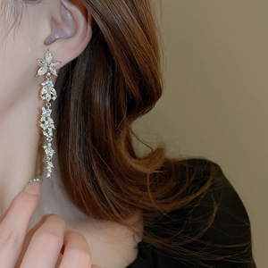 Detail of silver long tassel earrings with diamond-encrusted floral design on a model