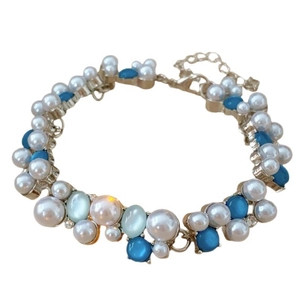 Bracciale vintage dorato con pietre occhio di gatto blu e perle bianche su sfondo bianco