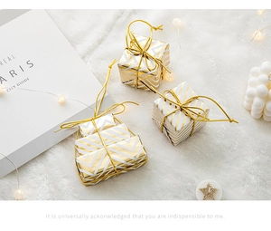 Close-up of golden striped mini gift box ornaments on a soft plush holiday background